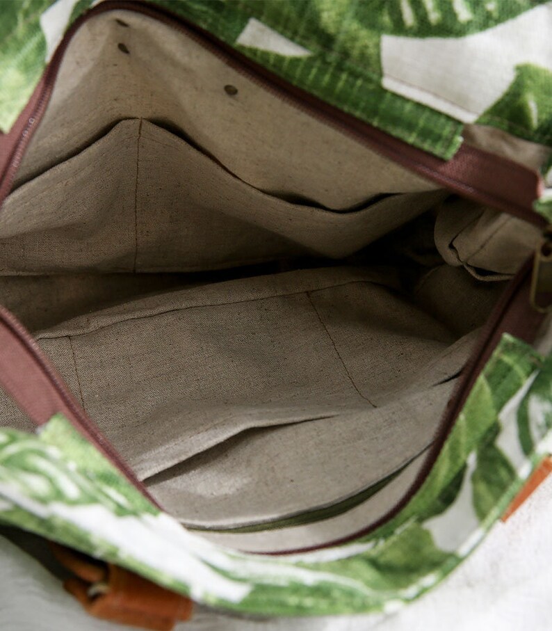 May include: The inside of a green and white tote bag with a brown zipper and a brown fabric lining. The bag has a small pocket on the inside.
