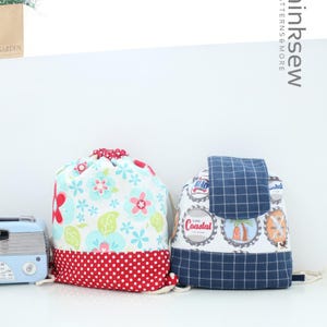 Op de afbeelding: Twee trekkoordtassen, een met een bloemen- en stippenpatroon en de andere met een blauw-wit geruit patroon en een kustthema. De tassen zijn gemaakt van stof en hebben een trekkoordsluiting.