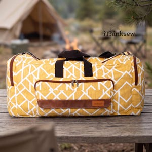 May include: A mustard yellow duffel bag with a white geometric line pattern, featuring dark brown fabric handles, brown zipper accents, and a front pocket with a brown leather-like patch labelled "handmade". The text "iThinksew" is visible.