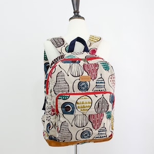 May include: A beige canvas backpack with a red zipper and a brown leather bottom. The backpack is decorated with a colorful pear pattern and the word "handmade" on a brown tag.