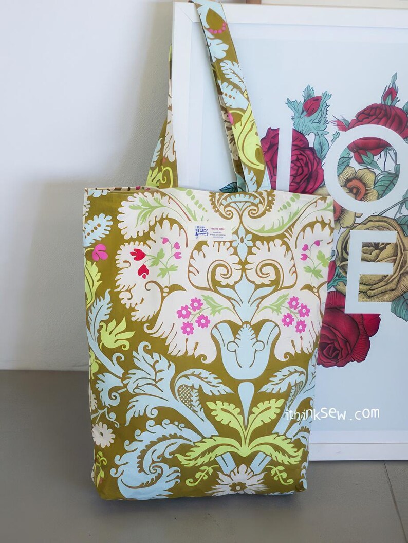 K&ouml;nnte beinhalten: Eine gr&uuml;ne Einkaufstasche mit Blumenmuster. Die Tasche hat ein wei&szlig;es Etikett mit dem Text "Made in Italy". Die Tasche liegt auf einer wei&szlig;en Oberfl&auml;che.