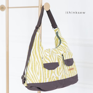 Pode incluir: Bolsa de ombro com estampa de zebra amarela e branca com dois bolsos frontais e base marrom. A bolsa tem uma alça marrom e fecho de zíper. O texto "ithinksew" é visível.