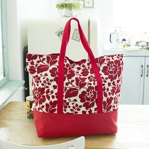 May include: A large red and white floral tote bag with a solid red bottom. The bag has two long red handles.