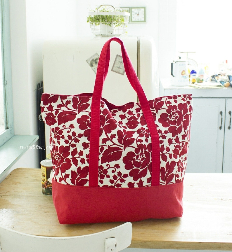 May include: A large red and white floral tote bag with a solid red bottom. The bag has two long red handles.