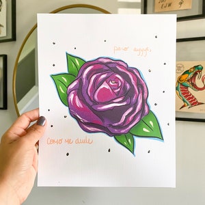 May include: A purple rose with green leaves and a white background. The text "pero ayyyy" and "como me duele" is written in orange on the print.