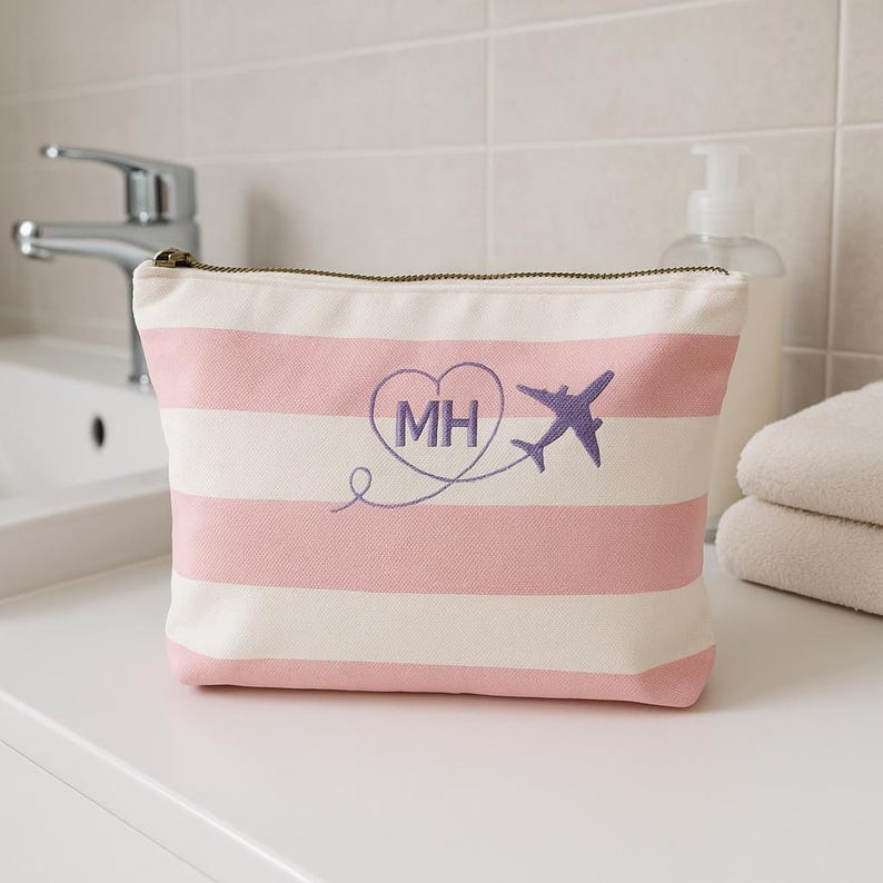 May include: Pink and white striped canvas cosmetic bag with a purple embroidered heart with the initials MH and a purple airplane flying out of the heart.