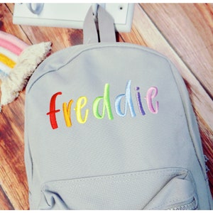 May include: A grey canvas backpack with a rainbow embroidered name "freddie" on the front.