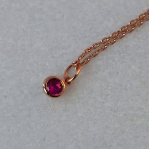 Puede incluir: Un delicado collar de cadena de oro rosa con un pequeño colgante redondo que presenta una gema rosa brillante.