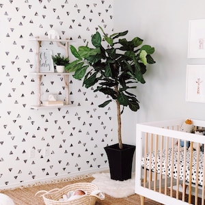 May include: A nursery with a white crib, a woven basket, and a large potted plant. The walls are decorated with a black and white triangle pattern. A small shelf displays decor, and the floor is covered with a woven rug.