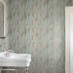 May include: A bathroom with floral wallpaper in shades of pink, purple, and cream on a light blue background. A white porcelain sink with chrome fixtures is in the foreground. A white door and mirror are also visible.