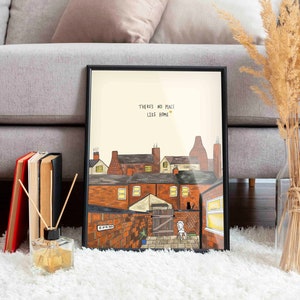 May include: A framed print with a black frame and a white background. The print features a hand-drawn illustration of a row of brick houses with a small garden at the back. The text "There's no place like home" is written in black at the top of the print.