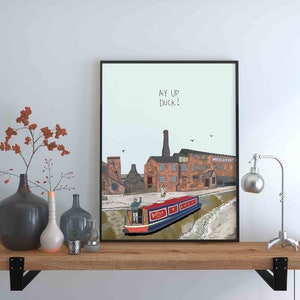 May include: A framed print with a light blue background featuring a cartoon illustration of a canal with a red and blue boat and a brick building with the text "AY UP DUCK!" and "MIDDLEPORT" in the background.