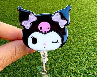 Pode incluir: Personagem de desenho animado preto e branco com laços rosa e uma caveira na cabeça. O personagem está preso a um porta-crachá retrátil.