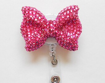 May include: A pink rhinestone bow attached to a clear plastic retractable badge holder.