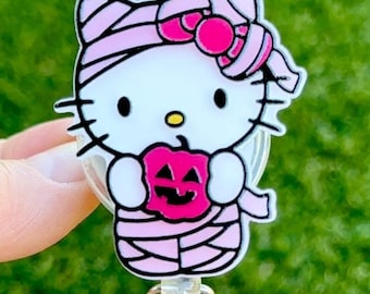 Pode incluir: Um porta-crachá retrátil de Hello Kitty com tema de Halloween rosa. Hello Kitty está vestida de múmia e segurando uma abóbora de Halloween.