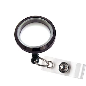 May include: Black metal locket with a clear glass insert, attached to a retractable badge holder with a clear plastic strap.