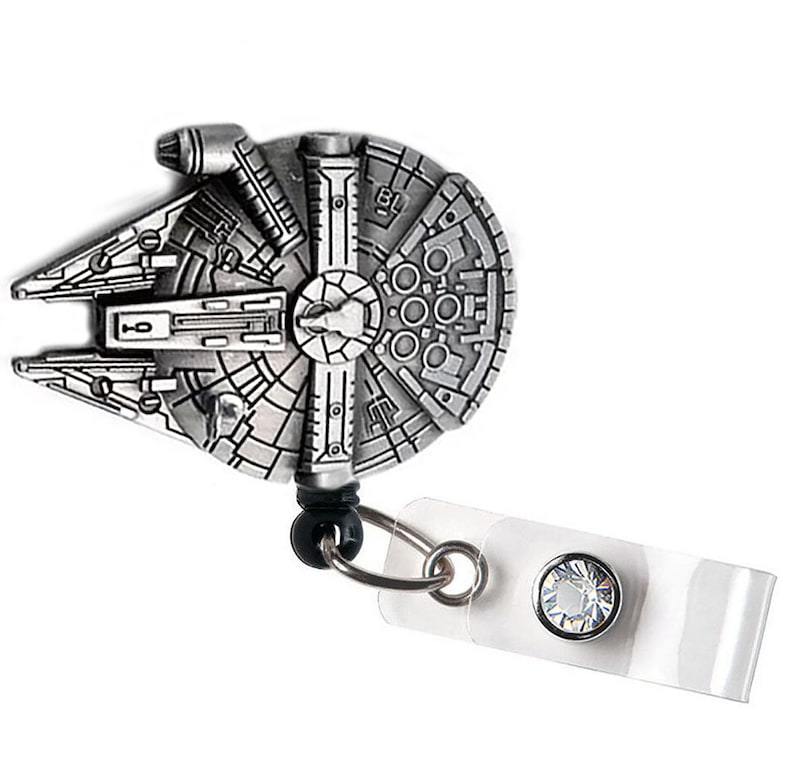 May include: A silver-toned Millennium Falcon charm attached to a clear plastic retractable badge holder with a clear rhinestone.