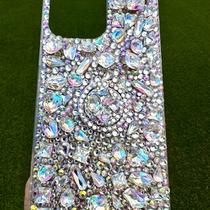 May include: A clear phone case covered in iridescent rhinestones of various shapes and sizes.