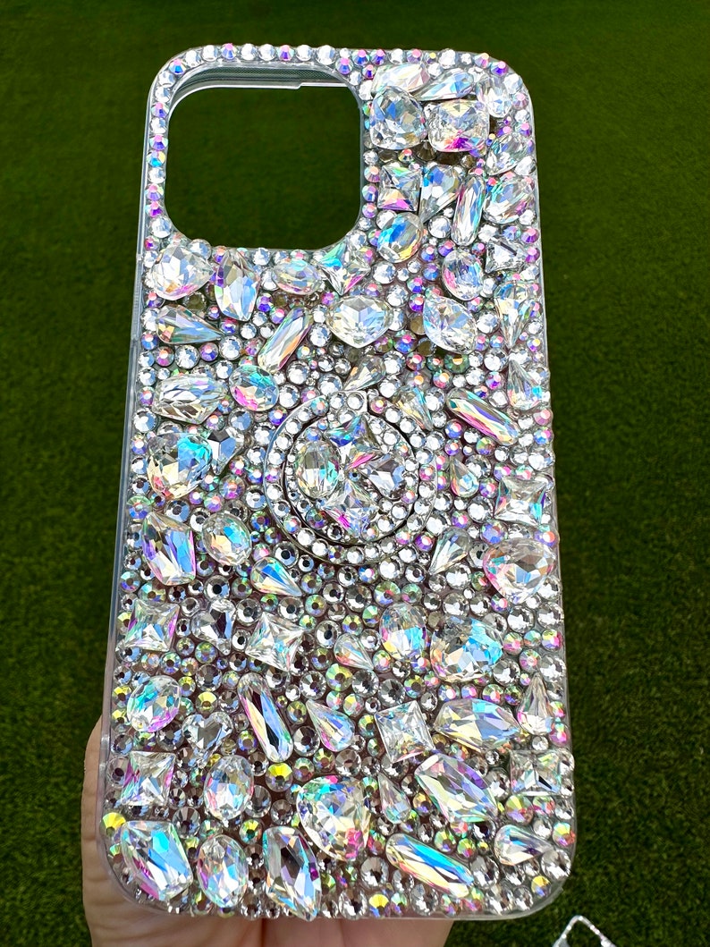 May include: A clear phone case covered in iridescent rhinestones of various shapes and sizes.