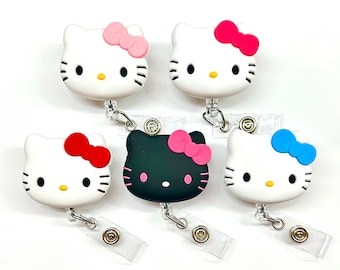 Pode incluir: Cinco porta-crachás retráteis Hello Kitty. Os porta-crachás são brancos com olhos pretos e bigodes. Cada porta-crachá tem um laço de cor diferente: rosa, vermelho, preto, azul.