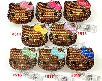 Pode incluir: Oito porta-crachás Hello Kitty marrons com laços de diferentes cores. Os laços são rosa, amarelo, roxo claro, verde claro, azul claro e azul. Cada porta-crachá tem um clipe de plástico transparente.