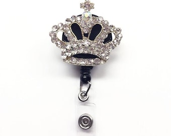 May include: A silver and black crown with clear rhinestones attached to a retractable badge holder.
