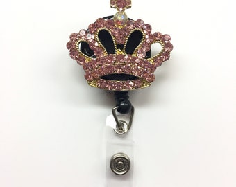 May include: A pink and gold rhinestone crown badge reel with a clear plastic badge holder.