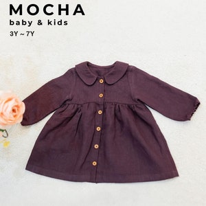 Könnte beinhalten: Ein dunkelviolettes Knopfkleid mit Peter-Pan-Kragen und langen Ärmeln. Das Kleid hat einen gerafften Rock und ist aus einem weichen, strukturierten Stoff gefertigt. Das Kleid ist mit "MOCHA baby & kids 3Y~7Y" gekennzeichnet.