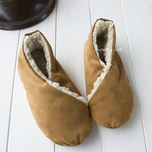 May include: A pair of brown suede slippers with a white faux fur lining. The slippers are folded over at the top and have a thinksew.com logo on the side.