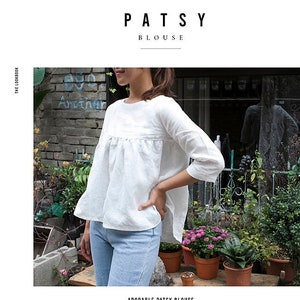 May include: A white blouse with a ruffled neckline and three-quarter sleeves. The blouse is loose fitting and has a relaxed, comfortable look. The text "PATSY BLOUSE" is at the top of the image. The text "ADORABLE PATSY BLOUSE" is at the bottom of the image. The text below the title describes the blouse's features and how it can be styled.