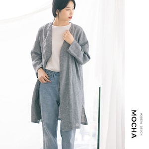 Pode incluir: Uma mulher vestindo um cardigã de linho cinza sobre uma camiseta branca e jeans azul. O cardigã tem um caimento longo e relaxado e uma gola ligeiramente aberta. O texto "MOCHA MODERN DESIGN" é visível no canto inferior direito da imagem.