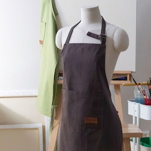 May include: A brown canvas apron with adjustable straps and a large pocket. The apron has a brown leather label with the text "The Maker" on it.