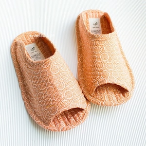 May include: A pair of orange fabric slippers with a white geometric pattern. The slippers have an open toe design.