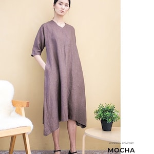 May include: A brown linen dress with a v-neck and a slightly asymmetrical hemline. The dress has a relaxed fit and is perfect for a casual summer look. The model is wearing black shoes with a small heel.
