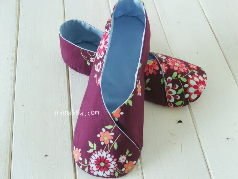 May include: A pair of burgundy fabric slippers with a floral pattern in shades of red, orange, and green. The interior is a light blue. The slippers are handmade and appear comfortable.