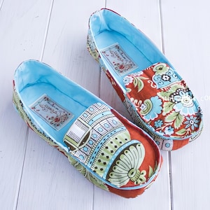 May include: Two pairs of fabric slippers with a blue lining and colorful floral patterns. The slippers have a red base and a blue trim.