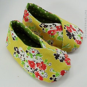 May include: A pair of yellow fabric slippers with a green and white floral print. The slippers are lined with a green fabric with white polka dots.