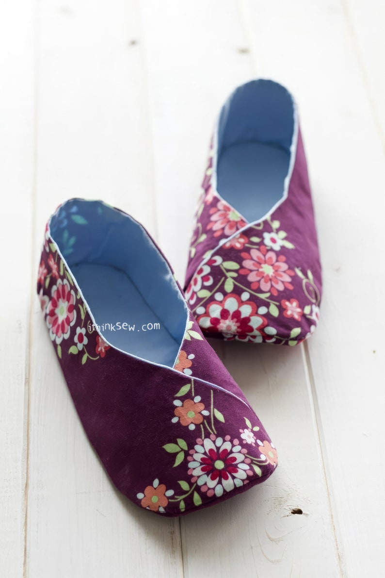 May include: A pair of handmade slippers with a floral pattern. The slippers are a deep purple with a light blue interior and a white trim. The floral design includes pink, red, and orange flowers with green leaves. The text "ithinksew.com" is visible.
