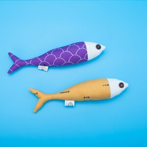May include: Two fabric fish toys. One is purple with white polka dots and the other is yellow with black dots. Both have white faces with black eyes.