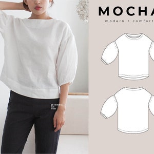 Puede incluir: Blusa blanca holgada de manga 3/4 con cuello redondo y mangas abullonadas. La blusa se muestra en una modelo con pantalones negros. El texto "MOCHA modern + comfort" se muestra en la esquina superior derecha de la imagen.
