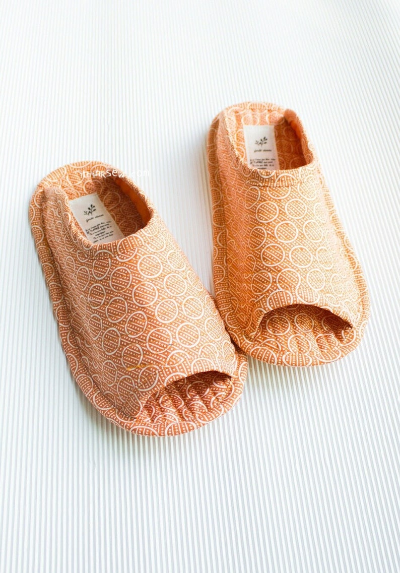 Op de afbeelding: Een paar oranje stoffen slippers met een wit geometrisch patroon. De slippers hebben een open teen.