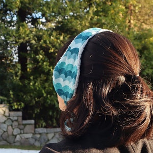 May include: A teal and white ear warmer with a wavy pattern. The ear warmer is made of fabric and has a soft, fuzzy lining.