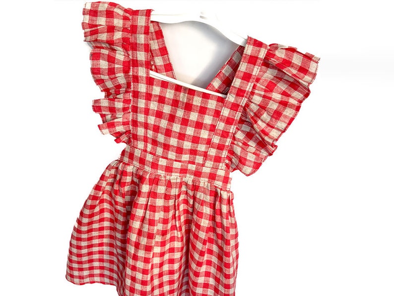 May include: A red and white gingham dress with ruffled sleeves. The dress has a sleeveless bodice and a gathered skirt.