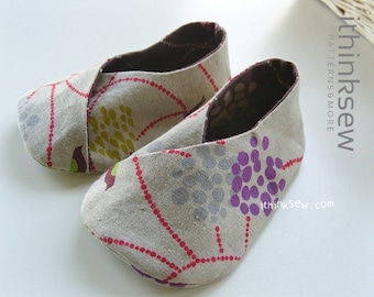 Pode incluir: Um par de sapatos de bebé bege com um design de tira cruzada. Os sapatos têm um estampado floral com detalhes roxos, verdes e vermelhos. Os sapatos são feitos de um tecido macio e confortável.