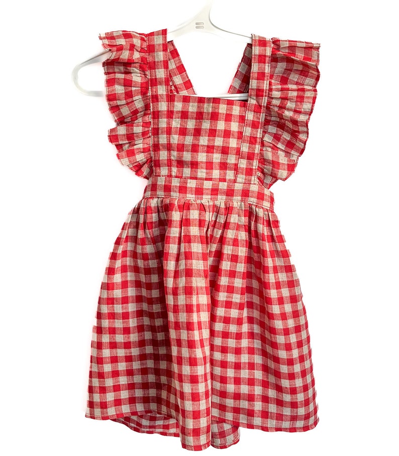 May include: Red and white gingham dress with ruffled straps. The dress has a sleeveless design and a full skirt.