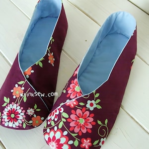 May include: A pair of burgundy fabric slippers with a floral pattern in pink, orange, and green. The interior is light blue, and the slippers have a wrap-around design. The slippers are designed for indoor use.
