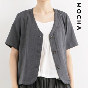 May include: A charcoal gray linen short-sleeved jacket with a v-neck and button closure. The jacket has a pocket on the left side and is worn over a white top.