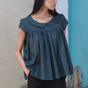 Op de afbeelding: Een tealblauwe blouse met een wit stippenpatroon en een witte Peter Pan-kraag. De blouse heeft korte mouwen en een geplooide bovenkant.