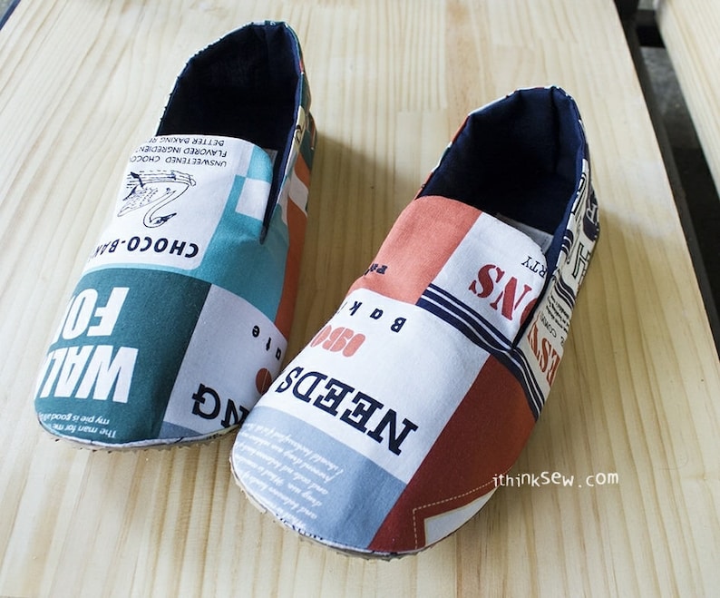 May include: A pair of blue and red fabric slippers with a patchwork design. The slippers have a variety of text printed on them, including "NEEDS", "BAK", "FO", and "CHOCO-BAN".