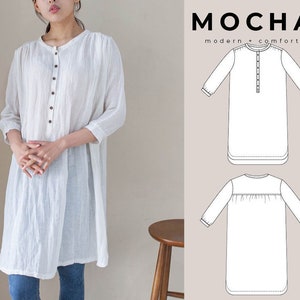 Może przedstawiać: Biała koszula z długimi rękawami, zapinana na guziki z przodu i lekko marszczona w talii. Koszula jest pokazana na modelce, a także jako rysunek liniowy.